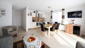 Ein modernes Wohnzimmer mit Essbereich, Küche und einem an der Wand befestigten Fernseher.