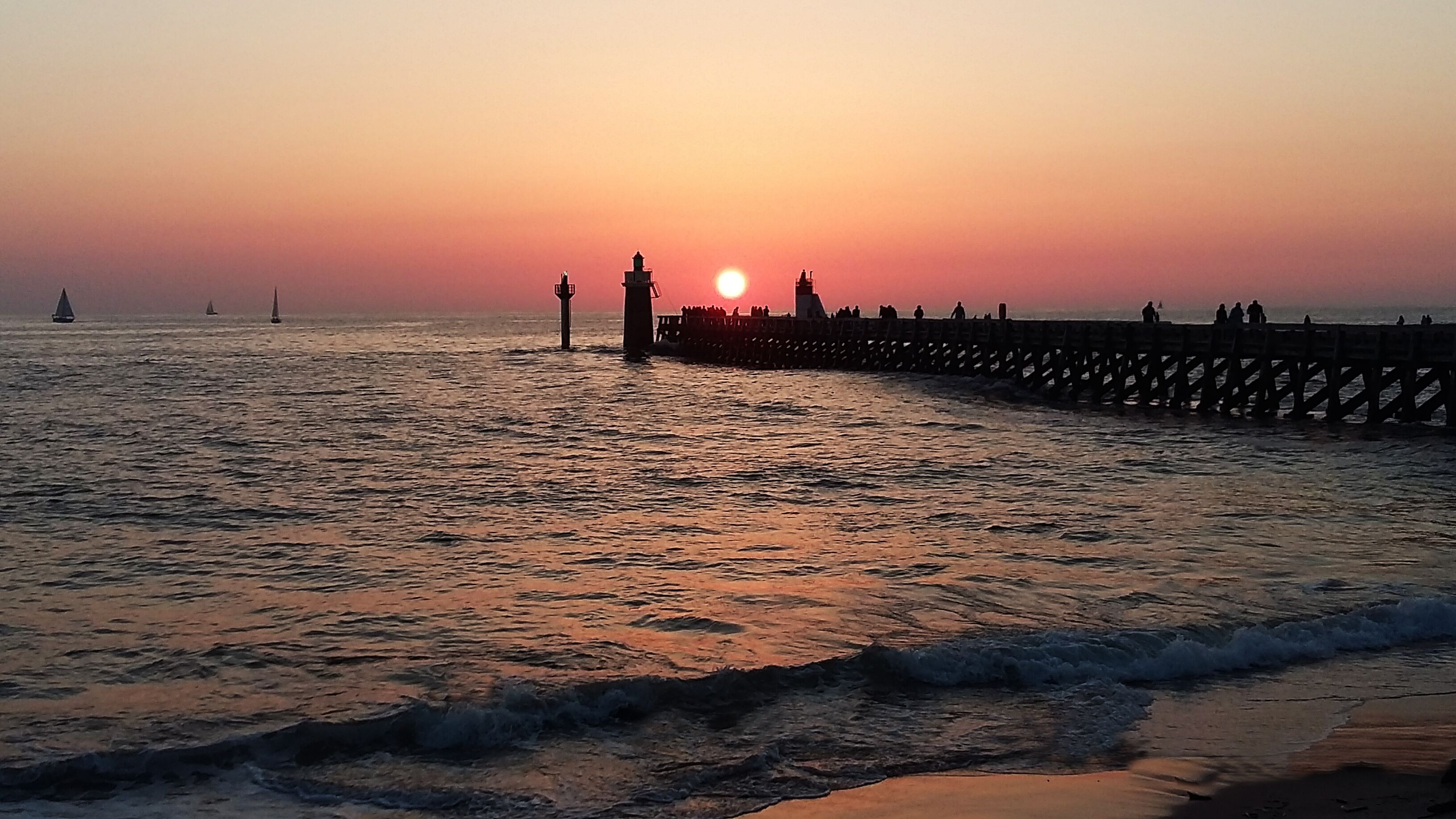 Een steiger die zich uitstrekt in de zee, met een zonsondergang op de achtergrond.