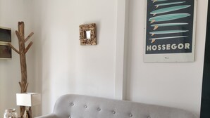 En ljusgrå soffa med klädsel i ett rum med trägolv, en inramad tavla på väggen och en lampa på ett sidobord.