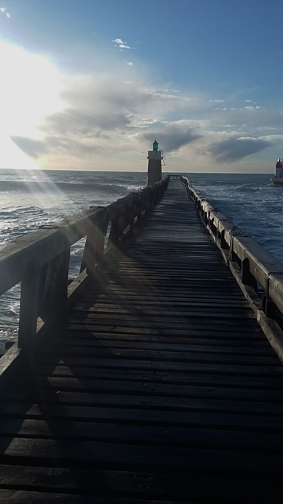A wooden pier extending into the sea with a lighthouse at the end.