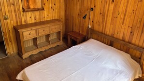 Ein Zimmer mit Holzboden, einem Bett, einer Holzkommode und einem kleinen Tisch.