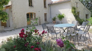 A courtyard with a round table and chairs, surrounded by potted plants and flowering bushes. - CHARMING HOUSE IN FORCALQUIER: Surrounded by nature, perfect for relaxation and activities with friends and family (Forcalquier)