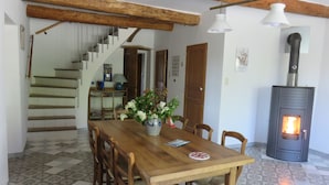 A dining area with a wooden table, chairs, a vase with flowers, a staircase, and a wood-burning stove. - CHARMING HOUSE IN FORCALQUIER: Surrounded by nature, perfect for relaxation and activities with friends and family (Forcalquier)