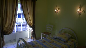 Een slaapkamer met een bed, een stoel, een raam met gordijnen en wandlampen.