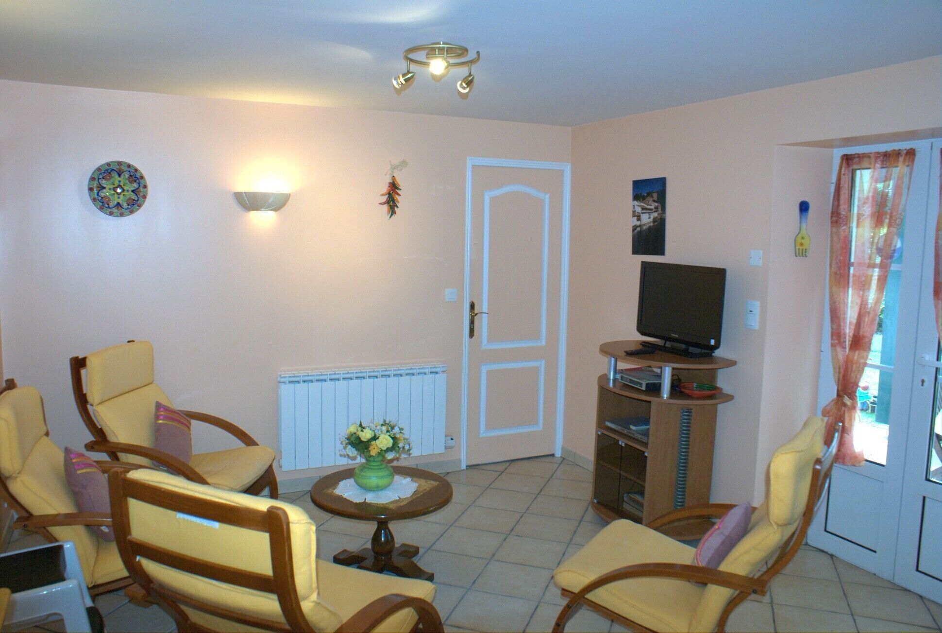 A living room with a television, two armchairs, a small table with a vase, and a radiator.