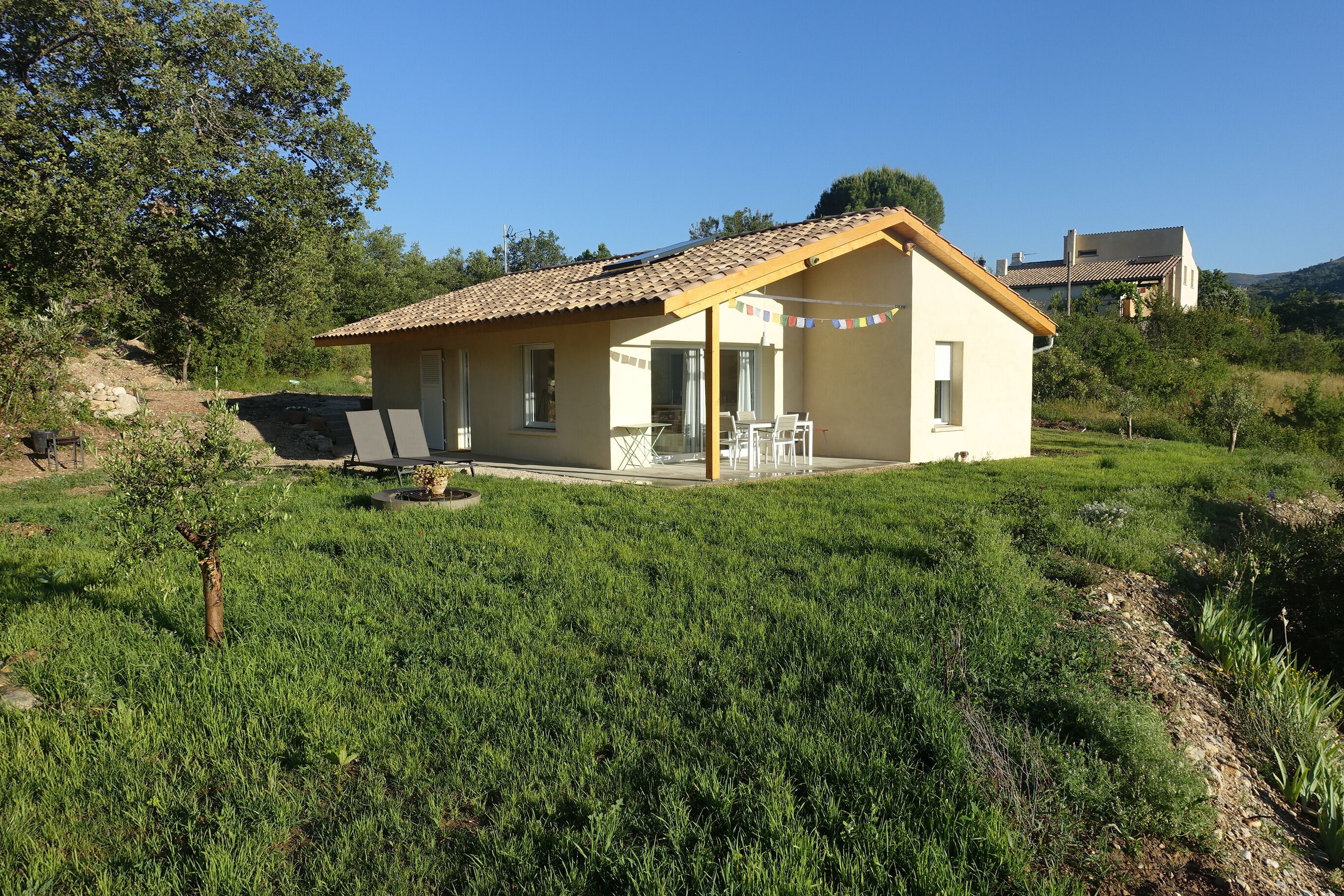 Une maison de plain-pied avec un toit en tuiles, une terrasse avec des meubles d’extérieur et une pelouse.