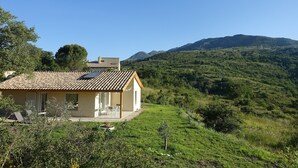 A house with a tiled roof, a patio with chairs, and a view of green hills and mountains. - Cottage pure nature, Provence, well being. (Digne-les-Bains)