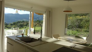 A modern kitchen with a large window, a sink, and a dining area with a table and chairs. - Cottage pure nature, Provence, well being. (Digne-les-Bains)
