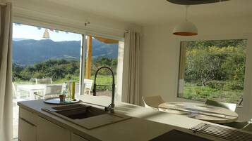 A modern kitchen with a large window, a sink, and a dining area with a table and chairs.