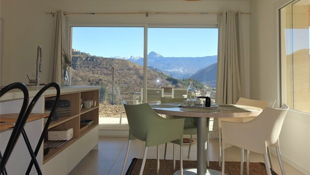 A modern kitchen with a dining area, large windows, and a view of mountains. - Cottage pure nature, Provence, well being. (Digne-les-Bains)