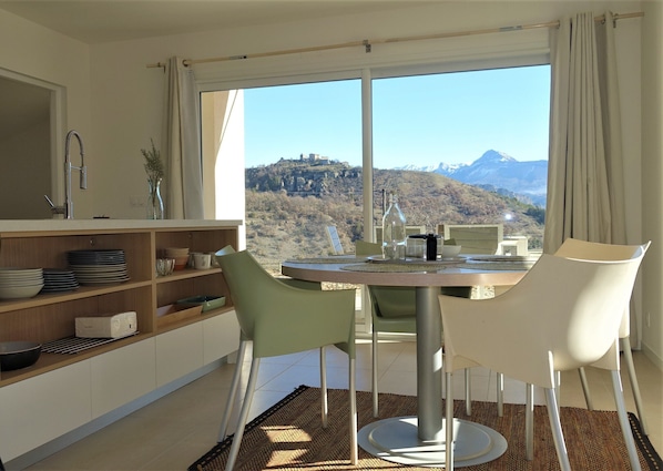 A modern kitchen with a dining area, large windows, and a view of mountains.