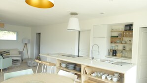 A modern kitchen with white cabinetry, a central island with a sink, and a dining area with a round table. - Cottage pure nature, Provence, well being. (Digne-les-Bains)