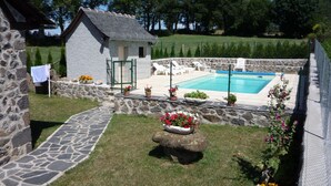 Una casa de piedra con piscina, rodeada por un muro de piedra y plantas en macetas.