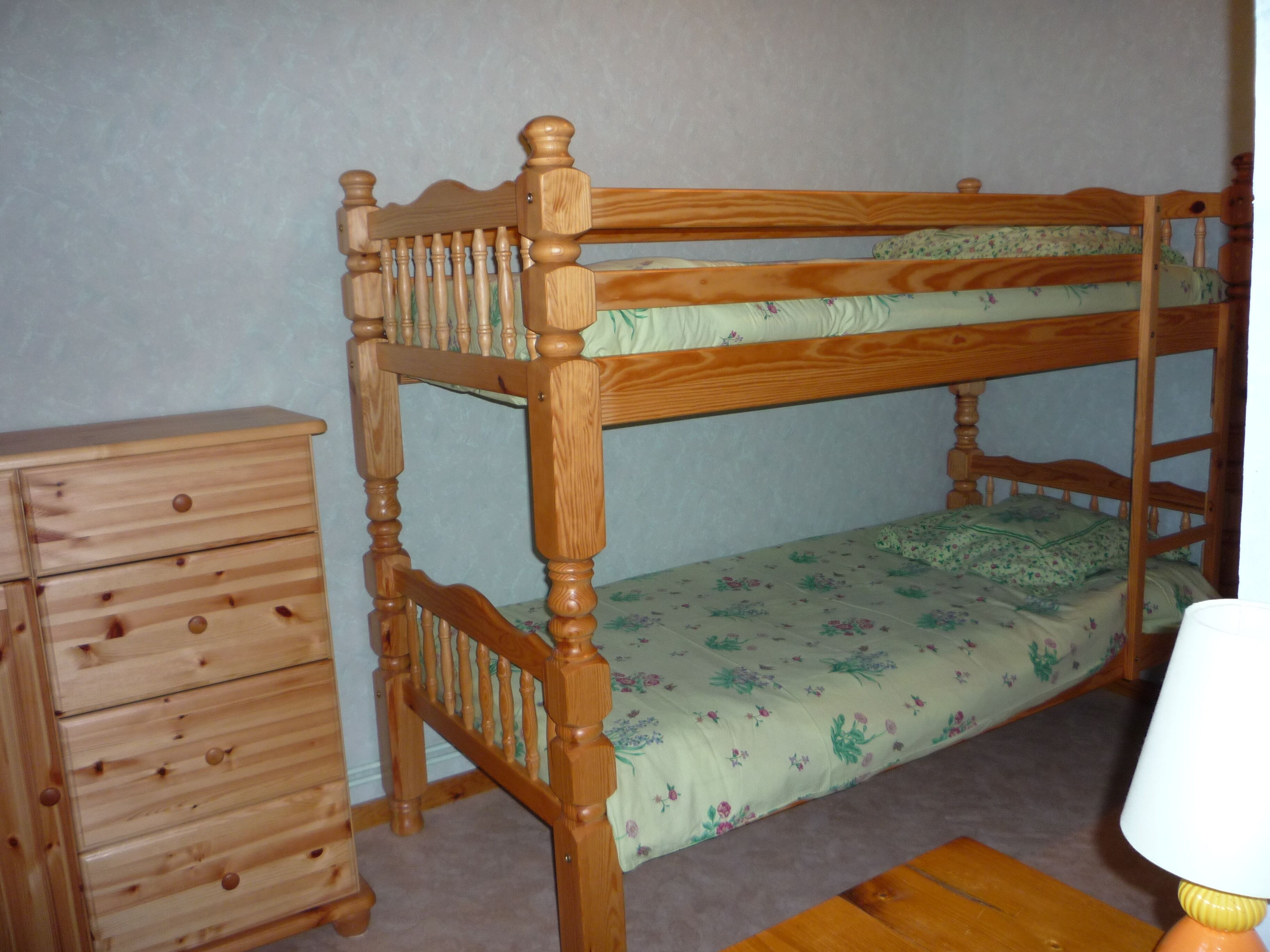 A bunk bed with a wooden frame and a floral bedspread.