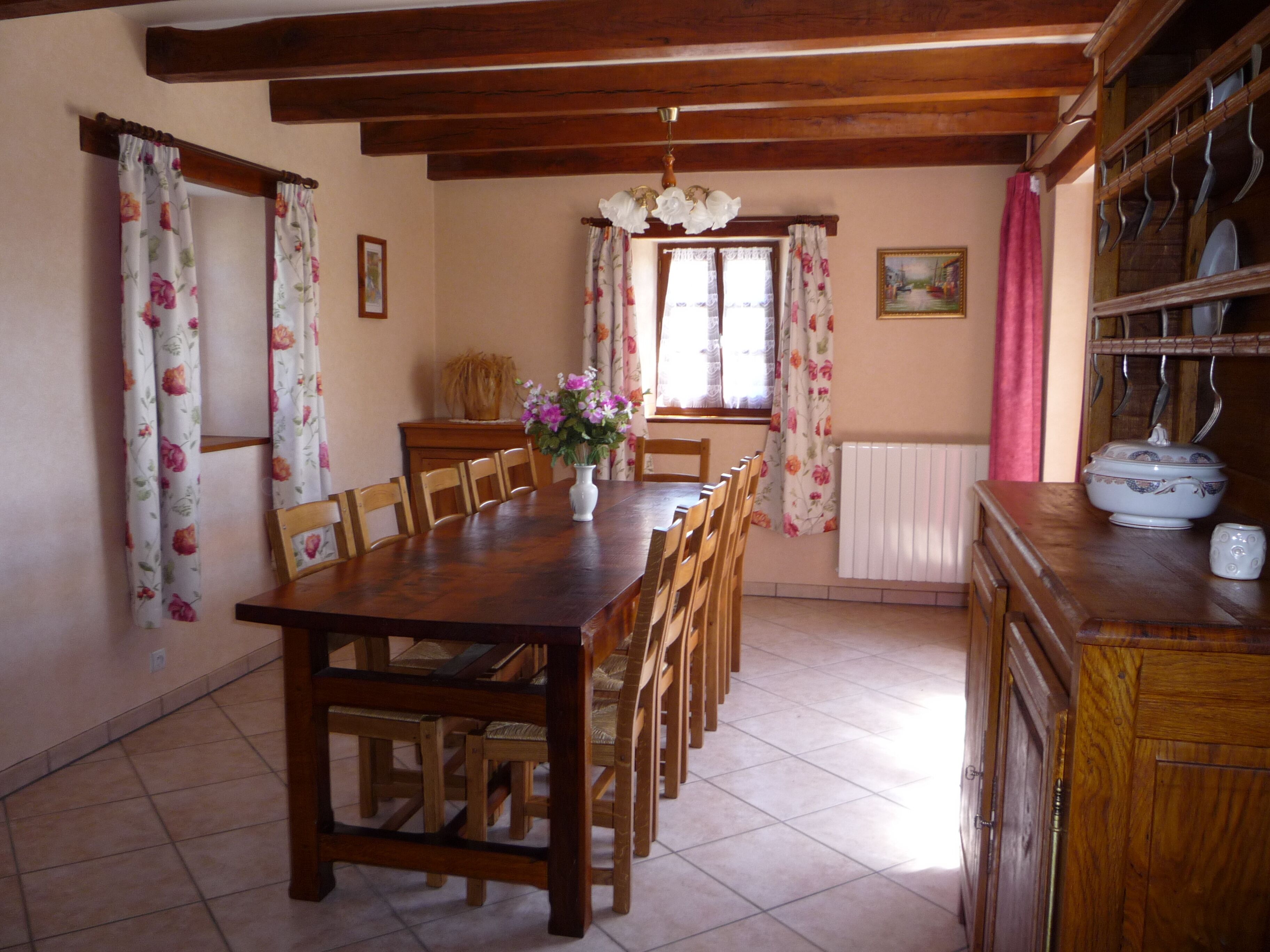 A dining room with a wooden table and chairs, a vase with flowers, and a window with curtains.