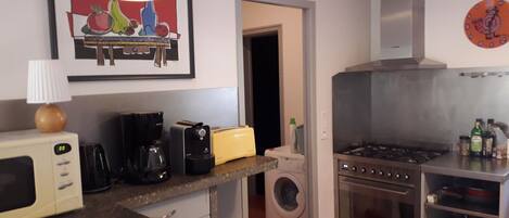 A compact kitchen with a microwave, toaster, and stove. There's a washing machine and a sink.