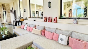 A modern living room with a large sectional sofa, a black coffee table, and a dining area visible through a large window. - A  prestigious and secluded Riad-style villa with HEATED POOL (Essaouira)