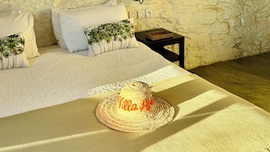 A bedroom with a stone wall, a bed with white linens, a small table with a lamp, and a straw hat on the bed. - A  prestigious and secluded Riad-style villa with HEATED POOL (Essaouira)