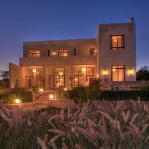 Une maison moderne à deux étages, dotée d’une façade en pierre, de grandes fenêtres et d’une entrée bien éclairée.
