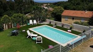 A swimming pool with lounge chairs, a fenced area, and a view of a coastal landscape. - 90m² between sea (2km) and mountains, in the heart of the maquis (Talasani)