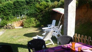 A patio with a table set for dining, surrounded by chairs, and a small garden area with a wooden fence and greenery. - 90m² between sea (2km) and mountains, in the heart of the maquis (Talasani)