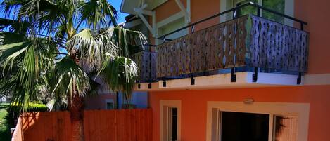 A two-story house with a balcony, a patio with furniture, and a fenced yard with a palm tree.