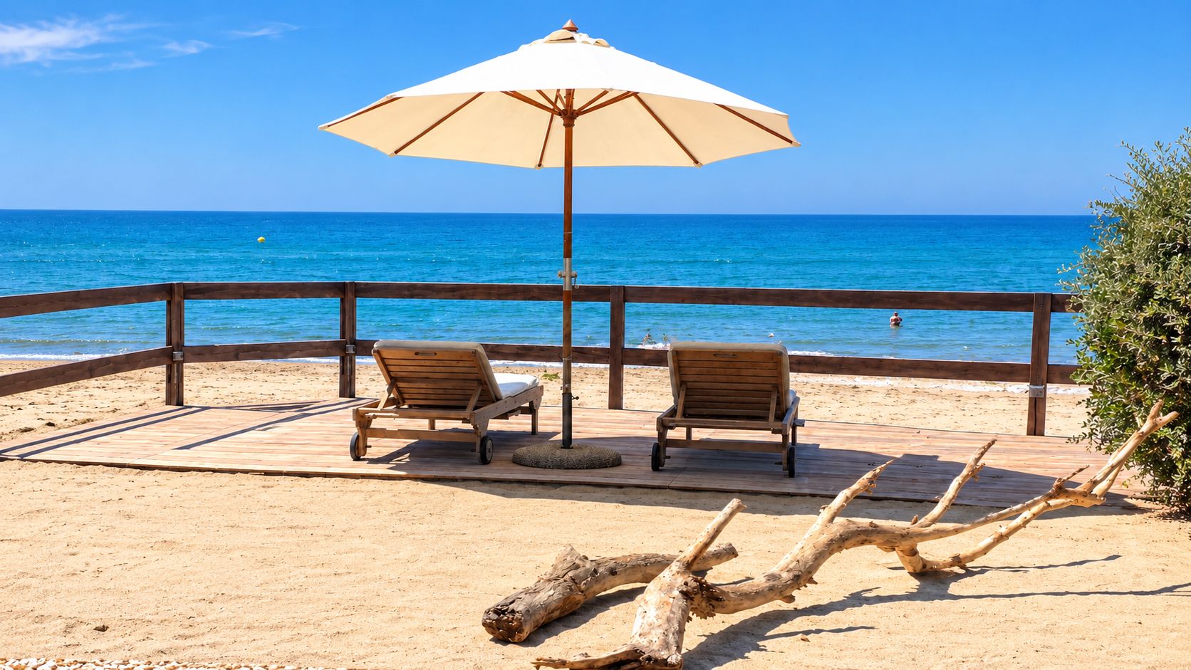A beachside lounge with two wooden lounge chairs and a large umbrella, overlooking the ocean.