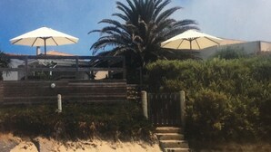 Uma praia com duas ombrelhas brancas, uma palmeira e uma escadaria que desce até a areia.
