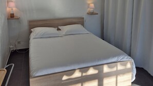 Siististi pedattu sänky, jossa on valkoiset lakanat, kaksi yöpöytävalaisinta ja puinen pääty.