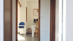 A hallway with a tiled floor leading to a room with a bed, a chair, and a table.