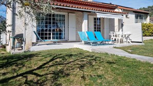 A house with a tiled roof, a covered patio with blue lounge chairs, and a white fence.