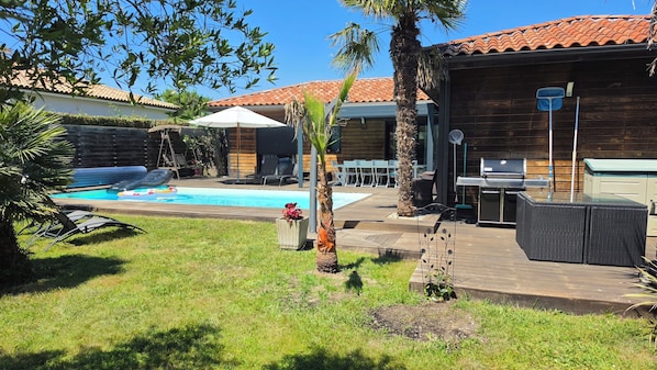 Un jardin avec une piscine, du mobilier d’extérieur, un barbecue et une terrasse en bois.