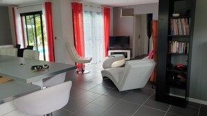 Een moderne woonkamer met een eethoek, een flatscreen televisie en een boekenkast.