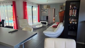 Een woonkamer met een bank, fauteuil, televisie en een boekenkast.