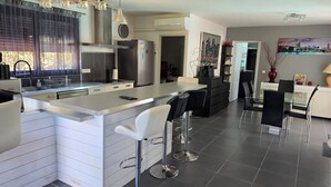Een moderne keuken met een centraal eiland, een bar met krukken, een eethoek met een glazen tafel en een zithoek met een bank en salontafel.