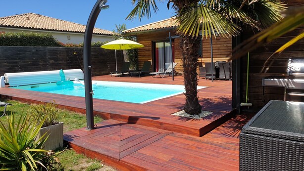 Een achtertuin met een zwembad, een houten terras, tuinmeubilair en een palmboom.