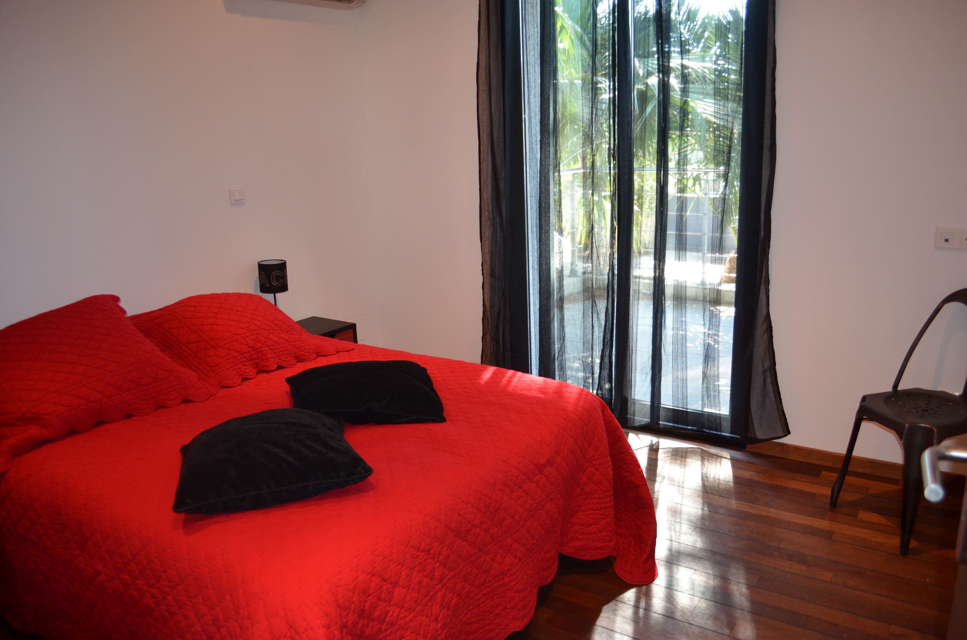 A room with a large bed, a nightstand, a chair, and a window with curtains.