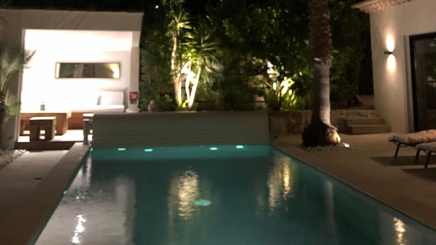 A nighttime view of a swimming pool with a palm tree and a building with a lit window.