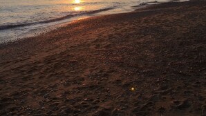 A beach with footprints leading to the water, a sunset in the background, and a distant hill.