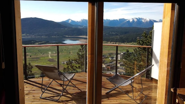 A balcony with two chairs and a view of mountains and a lake.