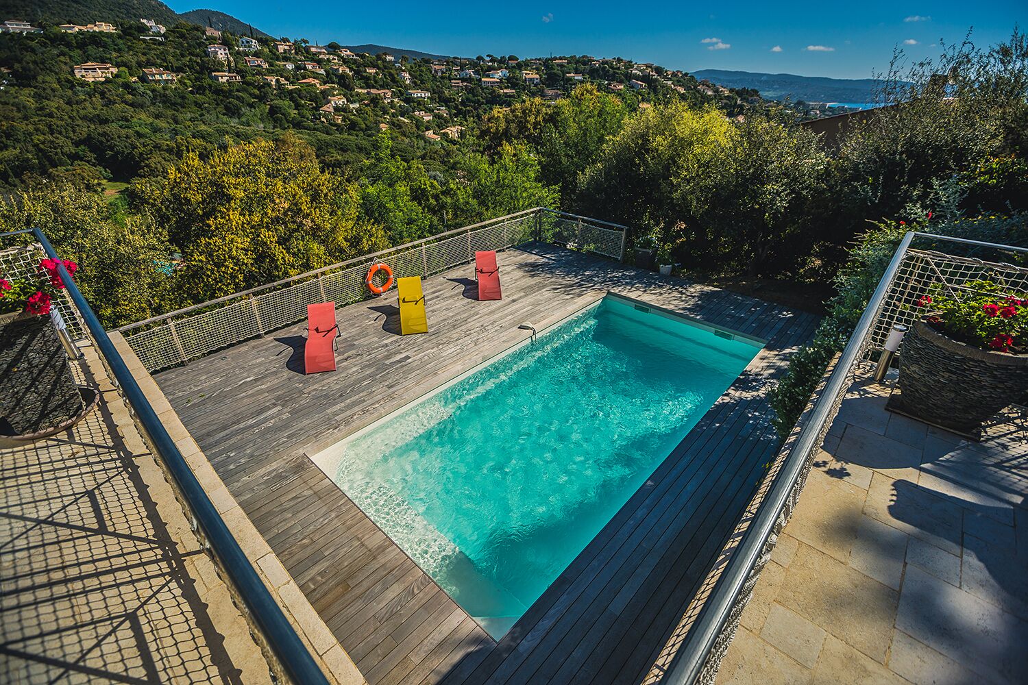 A rectangular swimming pool with a wooden deck, surrounded by a metal fence.