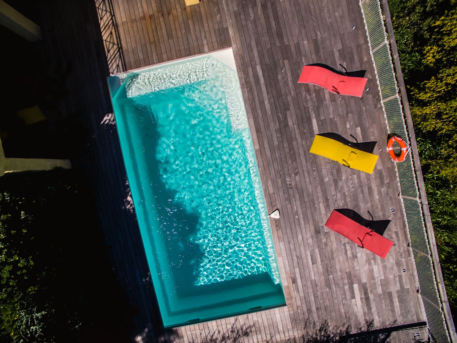 An aerial view of a rectangular swimming pool with a wooden deck surrounding it.