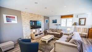 Una sala de estar moderna con una pared de piedra, un televisor de pantalla plana, un sofá, una mesa de centro y un mueble para televisión con lámparas.
