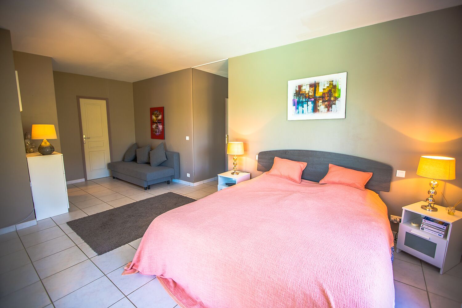 Un dormitorio con cama, mesitas de noche, un sofá y un cuadro en la pared.