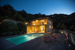 Une maison à deux étages avec une piscine, une terrasse en bois et un espace salon extérieur.