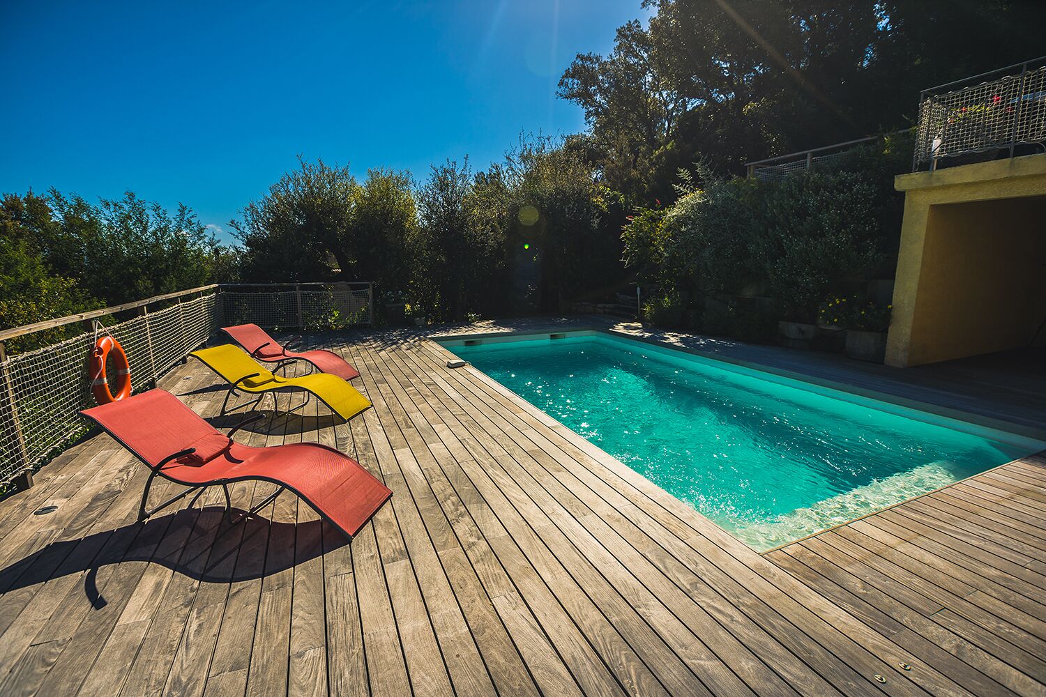A wooden deck with a swimming pool, surrounded by trees and a fence.