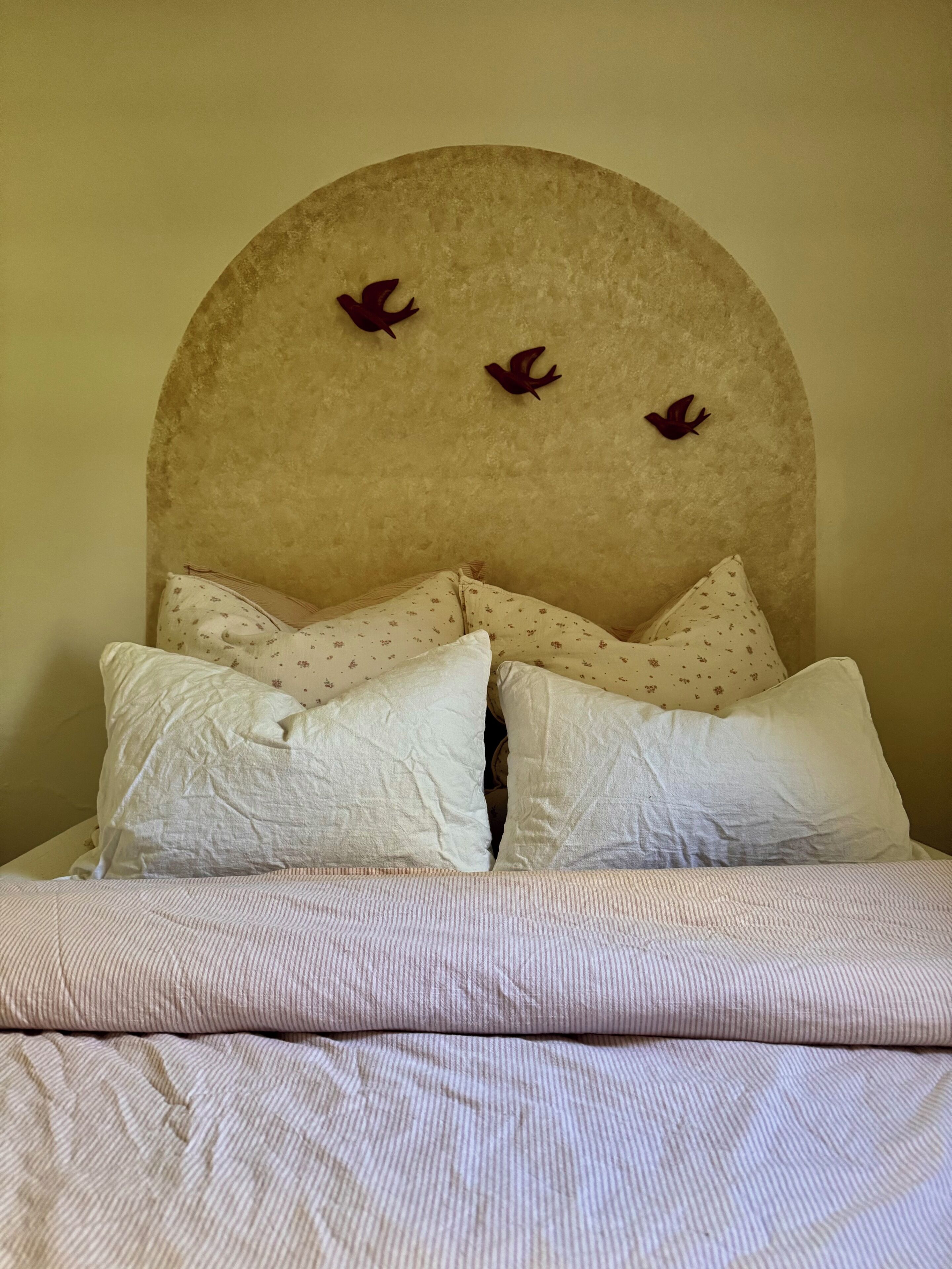 Un lit doté d’une tête de lit ornée d’un motif circulaire et de trois décorations représentant des oiseaux.