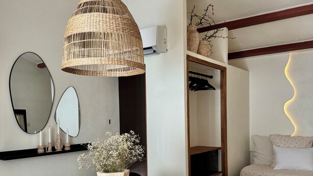 A dining area with a table set for four, a hanging wicker light fixture, a mirror, and a shelf with candles and a vase of flowers. - Le Nid des Baronnies: Rated 3-star vacation key! (Mirabel-Aux-Baronnies)