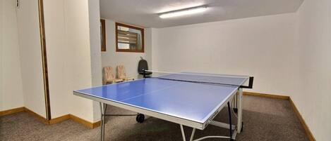 Une pièce avec une table de ping-pong, un sol recouvert de moquette, des murs blancs et une porte.