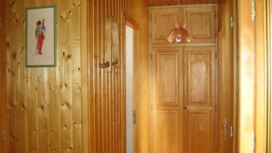 Puinen käytävä, jonka vasemmalla puolella on kehystetty taulu, oikealla puolella ovi, jossa on kello, ja katossa on valaisin.